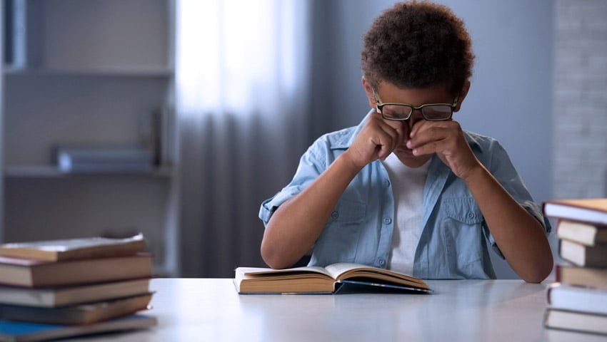 Criança com óculos analisando um livro próximo aos olhos, indicando possíveis problemas de visão.